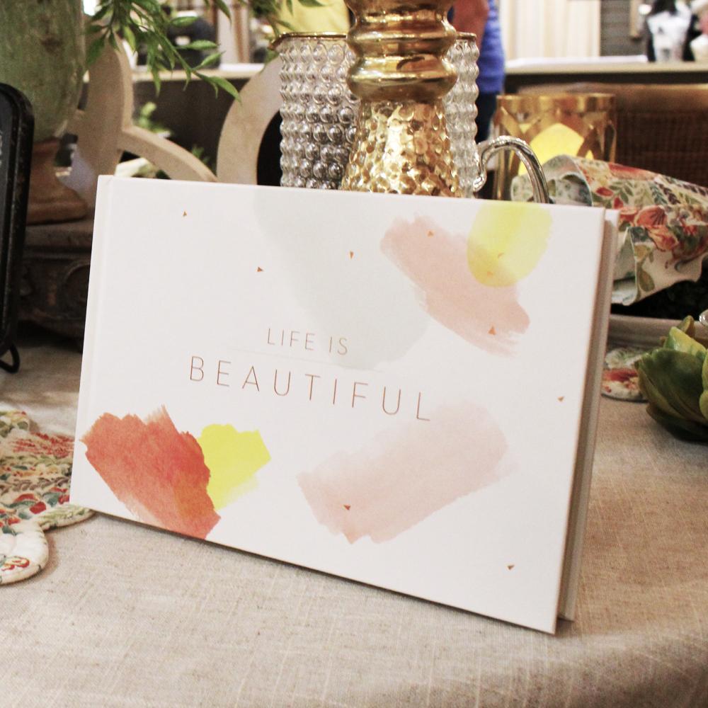 A book titled 'Life is Beautiful' on top of a table in front of candlesticks and place settings.