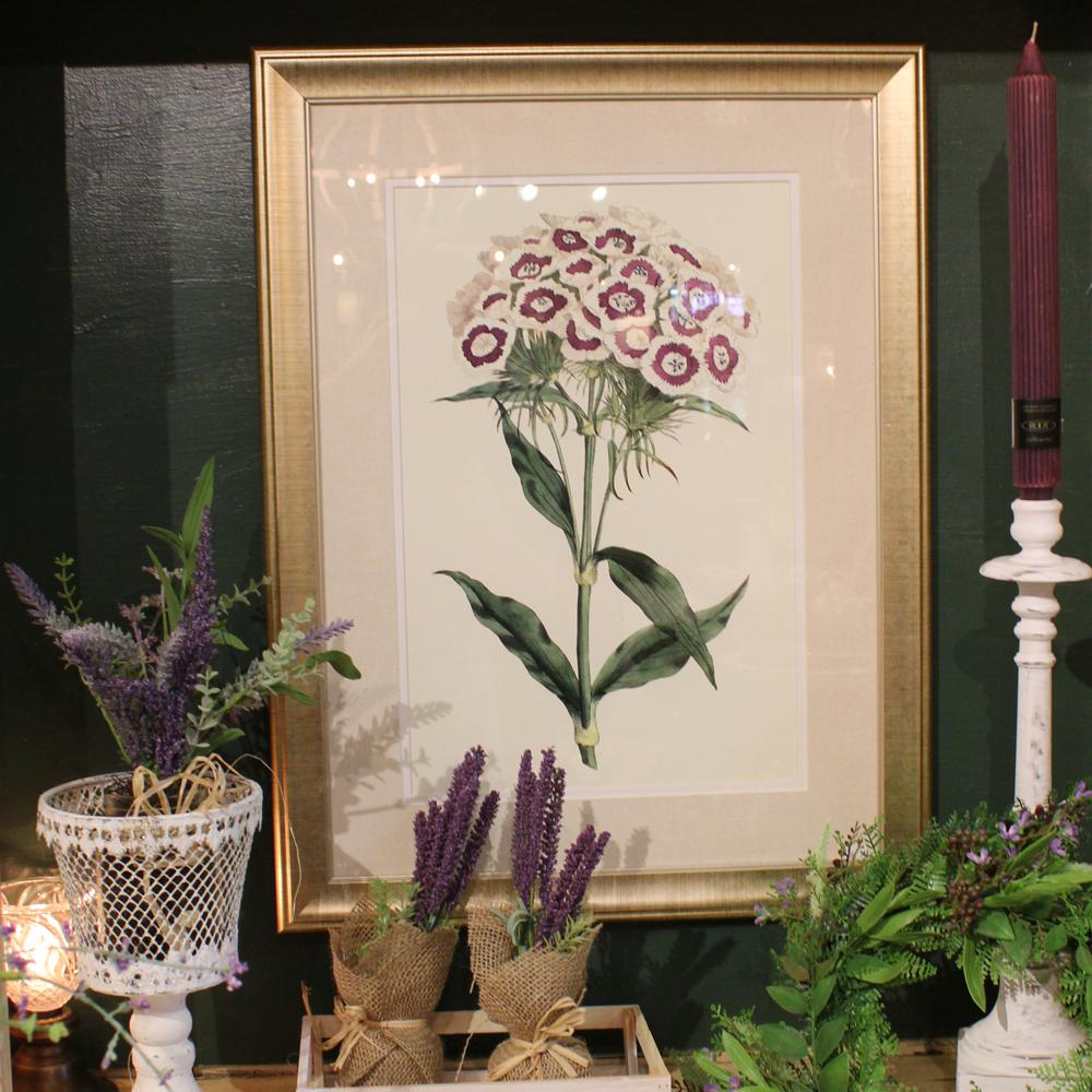 Framed floral art on a green wall with a variety of lavender and spring greens in front.