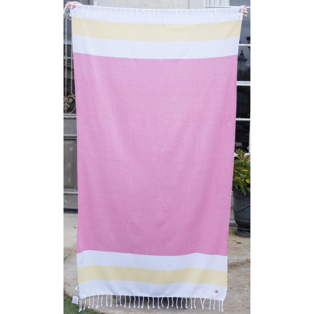 A pink beach towel with stripes at the top and bottom.  The stripes are wide and horizontal, white, yellow, white.  There is white fringe along the top and bottom of the towel.