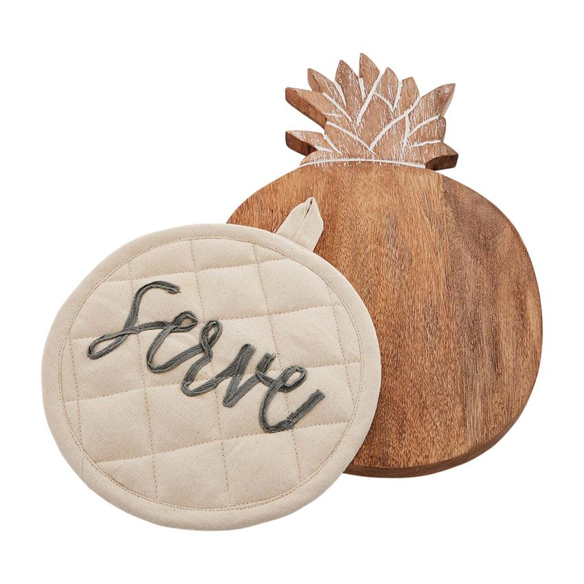 A round wooden trivet with engraved pineapple leaf detail at the top.  The engraving is white.  On top of the trivet is a round quilted off white potholder with embroidery that says 'serve' in cursive lowercase gray font.