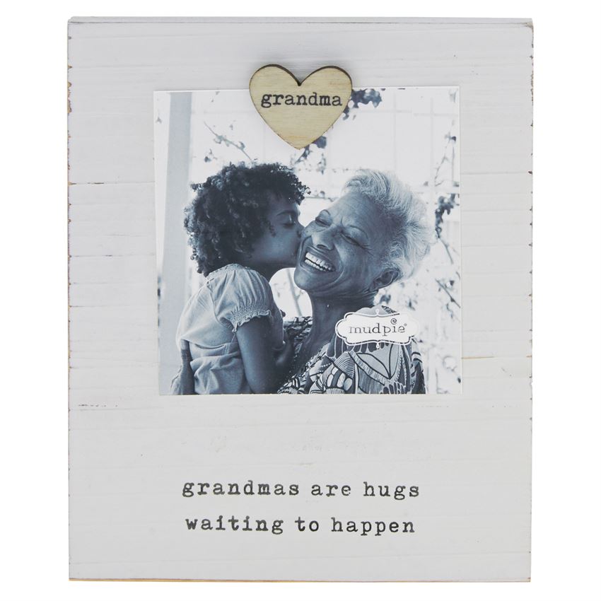 White wooden board with a heart shaped magnet that says 'grandma' on it.  The magnet holds a photo of a granddaughter and her grandmother above a printed saying 'grandmas are hugs waiting to happen'.
