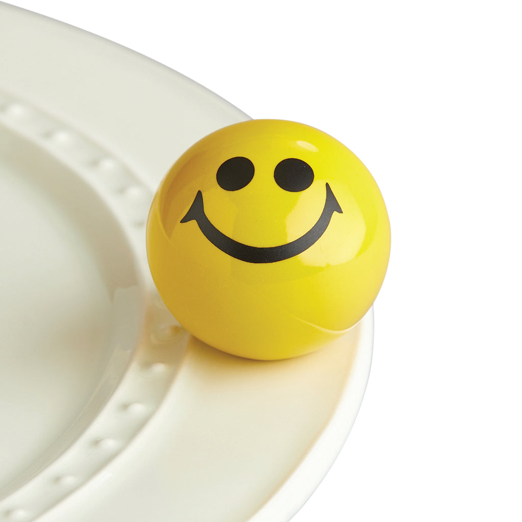 A yellow sphere with black eyes and a smiley face attached to the edge of a tray.