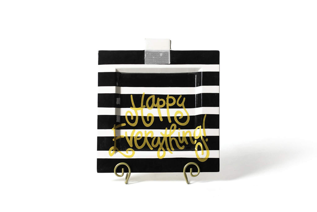 A square platter on a a gold scrolled plate stand.  The platter is black with thin horizontal white stripes, and 'Happy Everything' written in gold fun font across the bottom half.  There is a piece of square translucent velcro at the top middle of the platter to receive decorative attachments.