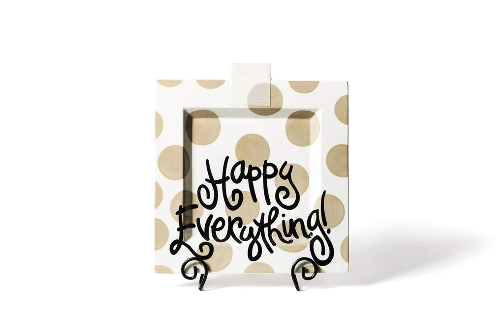 A square platter on a a black scrolled plate stand.  The platter is white with large tan dots, and 'Happy Everything' written in black fun font across the bottom half.  There is a piece of square translucent velcro at the top middle of the platter to receive decorative attachments.