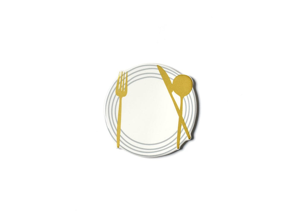 A flat ceramic cutout of a white dinner plate, with tan rings around the edge, and a gold fork on the left, and gold knife and spoon on the right.