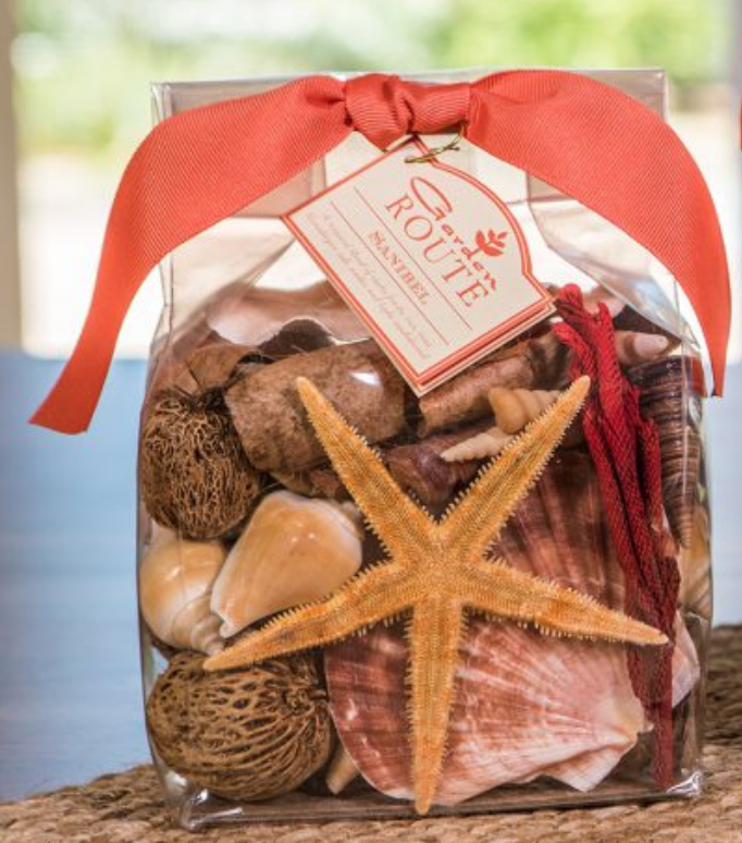 A bag of potpourri with starfish, shells, and a variety of other beach themed dried items.  Bag is clear with a coral colored fabric ribbon to close it.