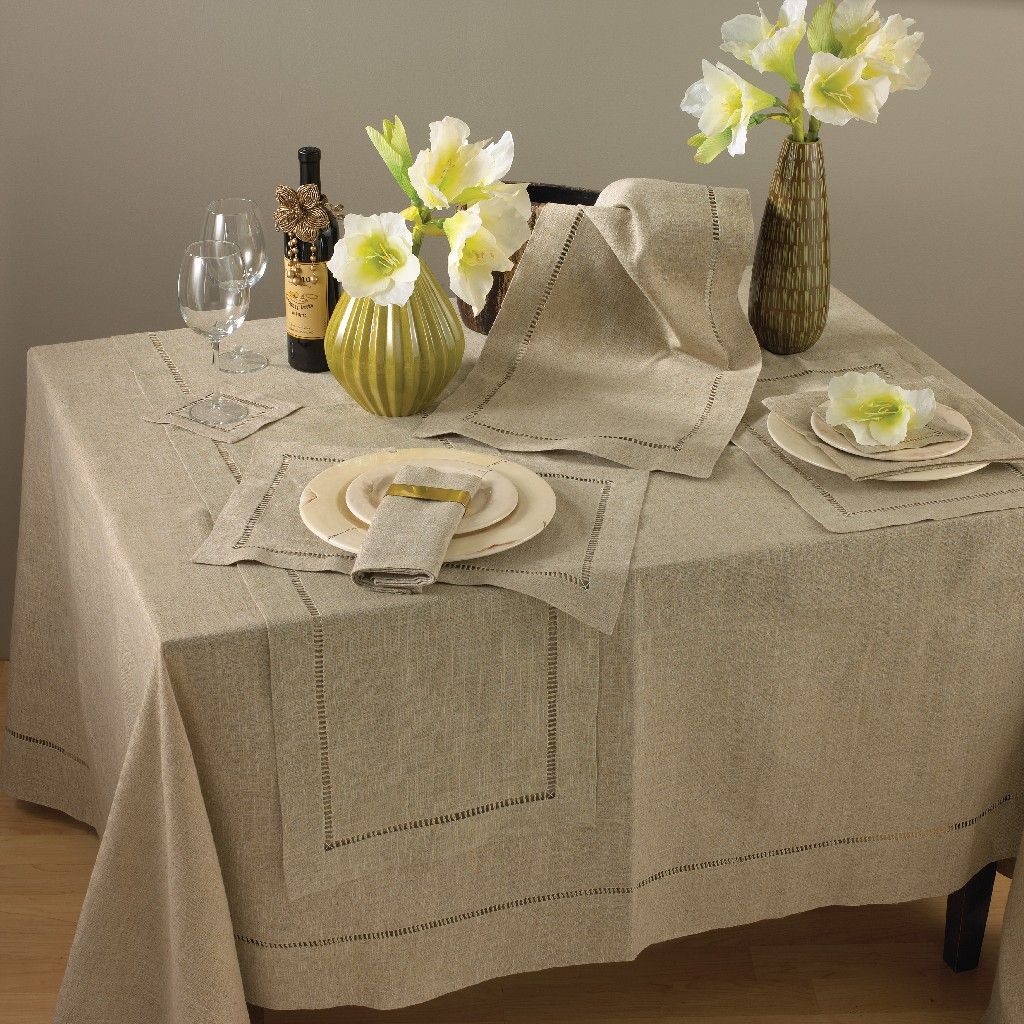 A table decorated with coordinating table cloth, runner, placemat and napkins.  All are neutral linen and have a hemstitched detail within the border.  Two vases, a bottle of wine and glasses finish the table.