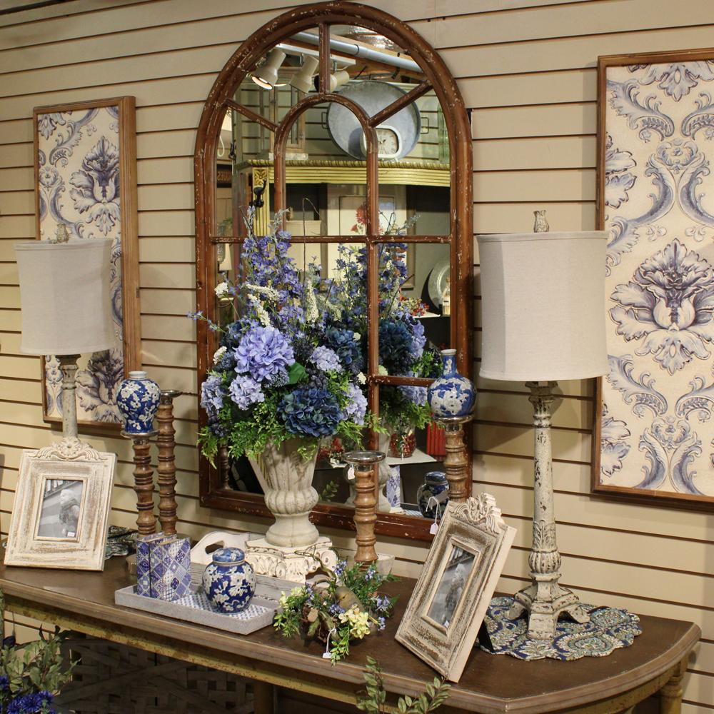 A collection of blue and white themed decor around a large mirror.  Floral arrangements, picture frames, lamps, and vases.