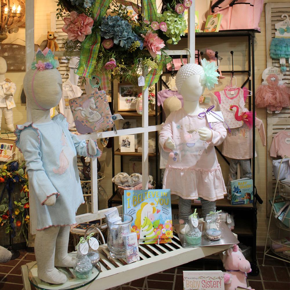 A display of kids clothing on mannequins surrounded by assorted toys, books, and accessories for boys and girls.