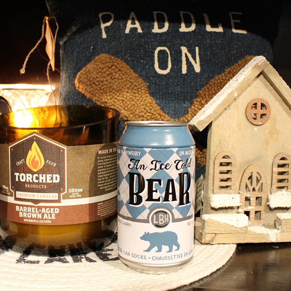 A multi wicked candle, socks in a beer can, and a decorative wooden Christmas house sit in front of a pillow that says 'Paddle On'