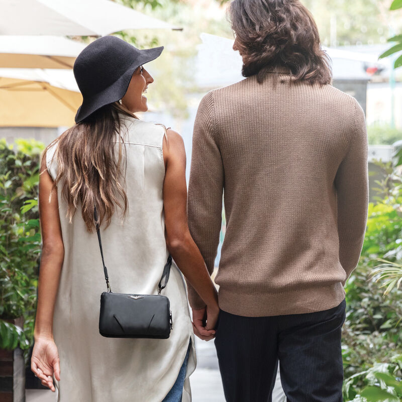 A photo of a woman and man holding hands as seen from the back.  She has a cross body purse worn low across her back.  