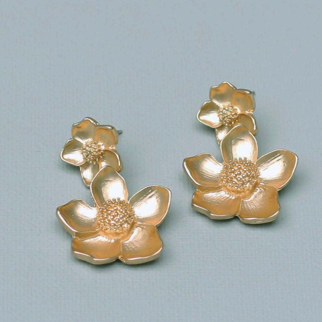 A photo of a pair of gold floral earrings.  Each earring has a large 5 petal flower below a smaller five petal flower.