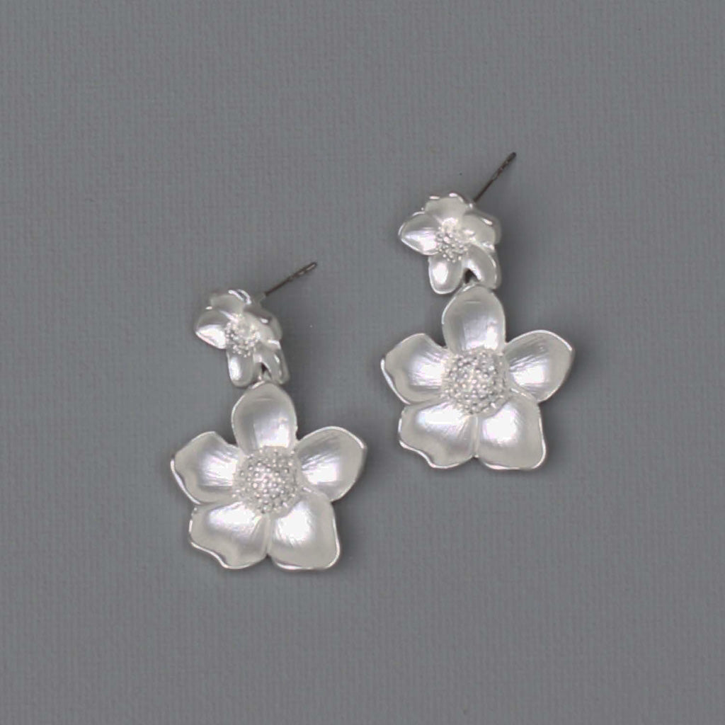 A photo of a pair of silver floral earrings.  Each earring has a large 5 petal flower below a smaller five petal flower.