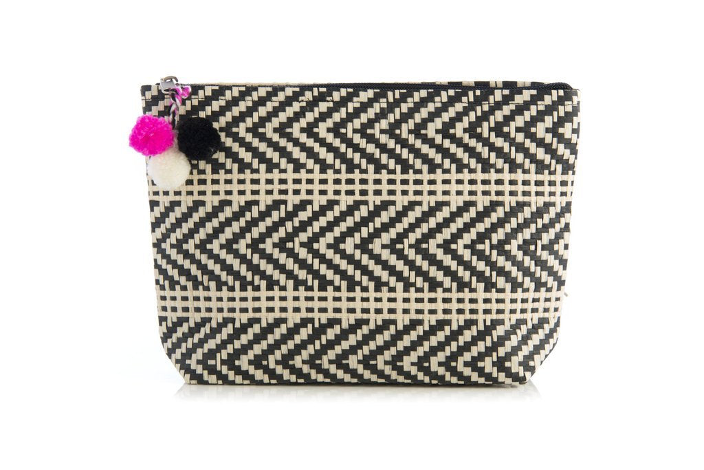 A black and white woven pouch on a white background.  The pattern of the weave alternates between a diagonal < and horizontal lines.  Attached to the zipper are three poms, black white and pink.