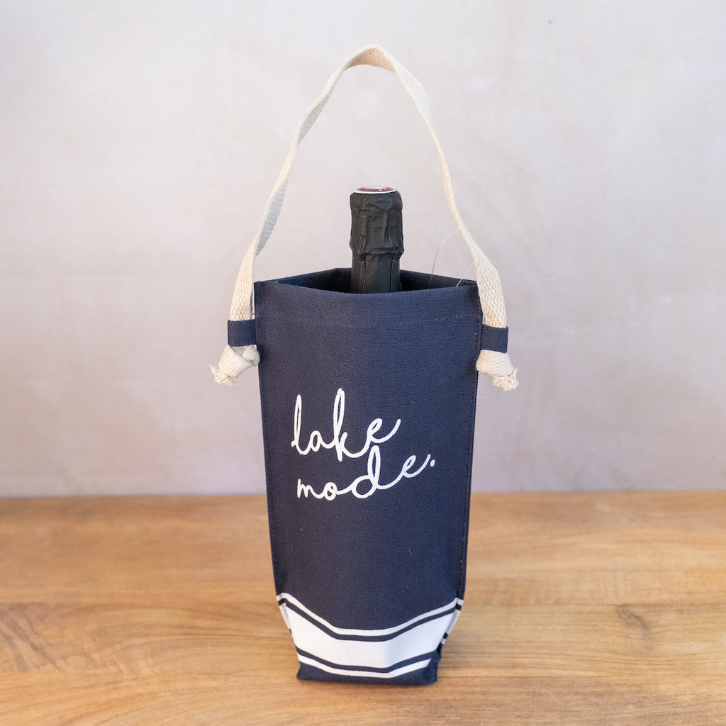 A navy blue canvas bag with white stripe at the bottom.  The handle is a wide jute strap.  Inside the bag is a bottle of champagne.