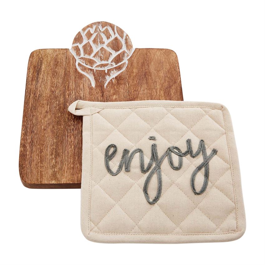 A square wooden trivet with engraved artichoke detail at the top.  The engraving is white.  On top of the trivet is a quilted off white potholder with embroidery that says 'enjoy' in cursive lowercase gray font.