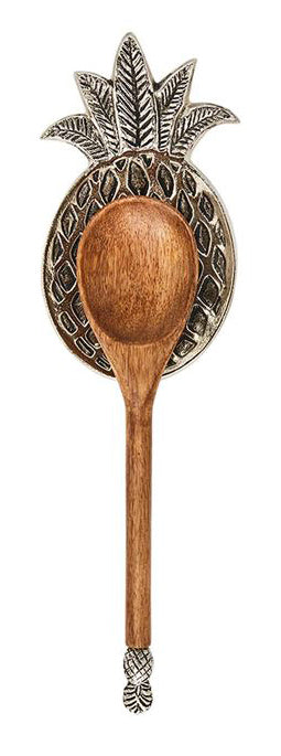 A metal spoon rest in the shape of a pineapple with recessed details.  A wooden spoon is resting on it and has a pineapple detail at the end of the spoon.