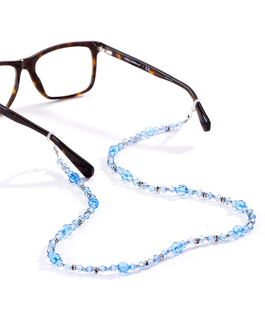 A blue crystal lanyard attached to a pair of tortoise shell glasses.  The angle of the image is from the back of the glasses and the lanyard is in the foreground.