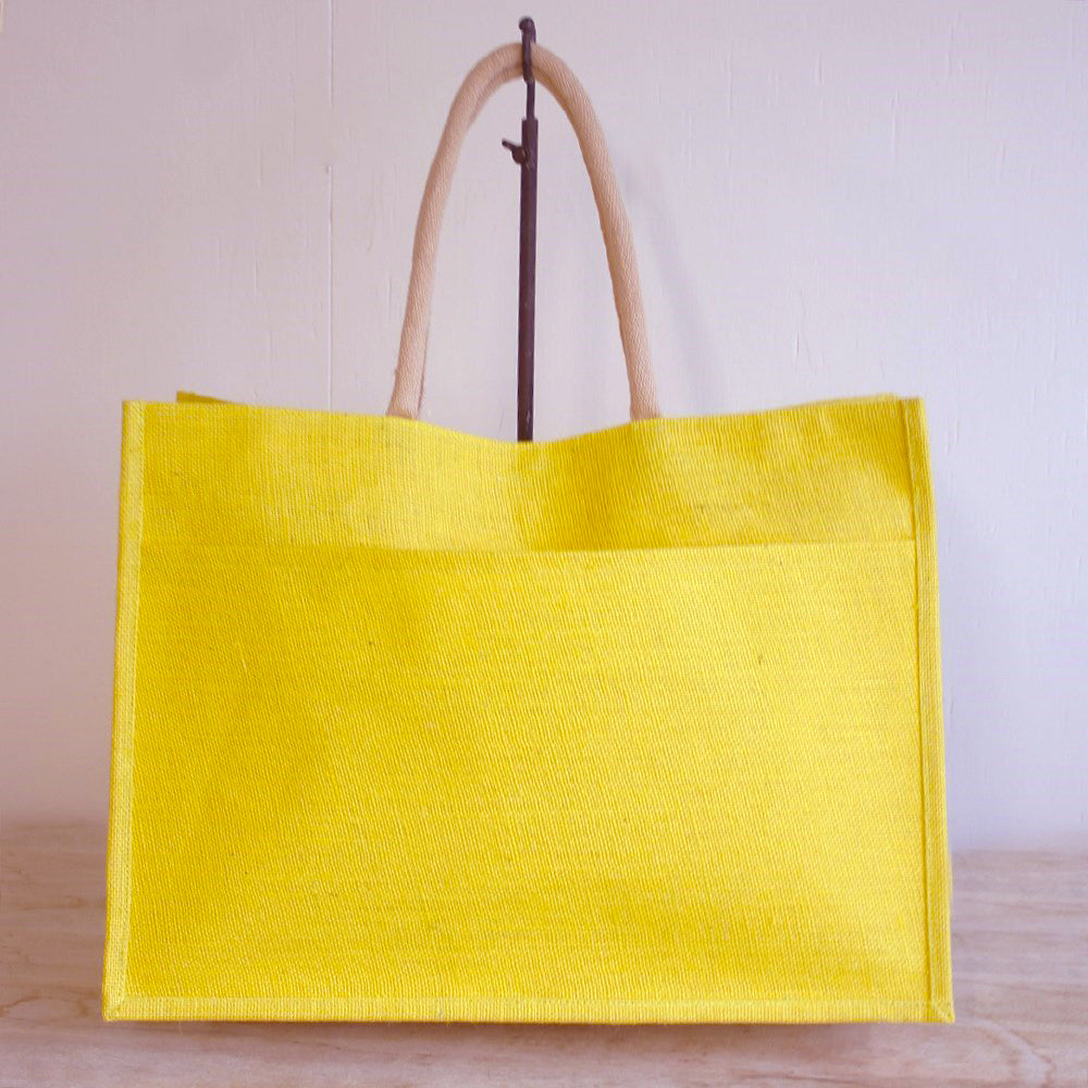 A lemon yellow jute tote with an outside pocket, suspended from a hook by its natural jute handles.