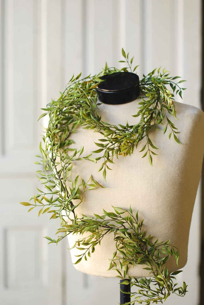 A fabric mannequin chest with a 6' long artificial smilax garland draped around it.
