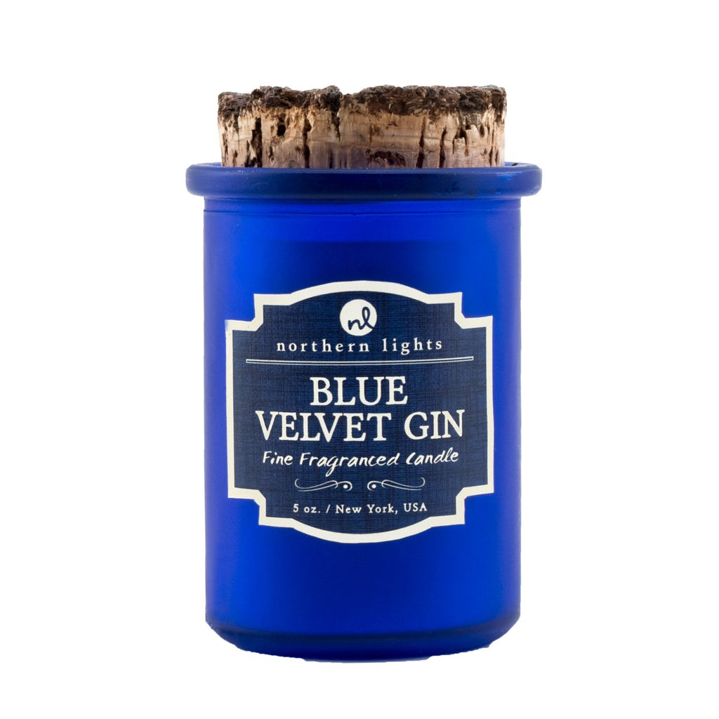 A blue frosted glass jar candle on a white background.  The lid is a piece of burnt cork.  The label is blue with a cream border and says 'Northern Lights  Blue Velvet Gin  Fine Fragranced Candle 5 oz. New York, USA'