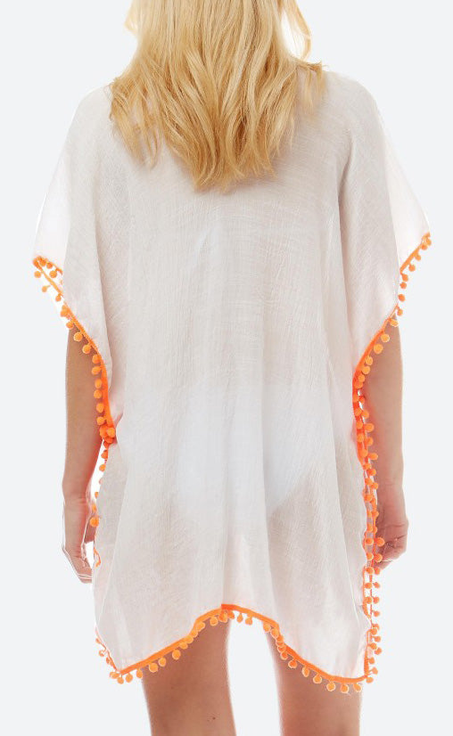 View of the back of a model wearing a loose fitting white top.  The bottom and arm are accented with orange pom pom trim.