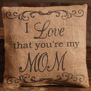 A burlap pillow that has curvy scroll work printed at the top and bottom of the front.  In the middle of the pillow it says ' I Love that you're my MOM' in matching black ink