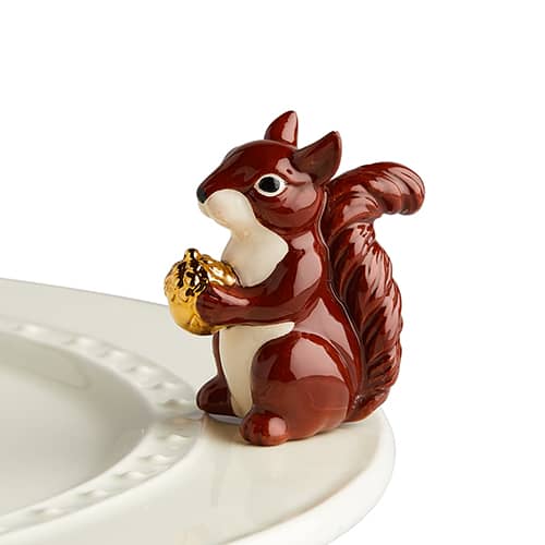 a ceramic squirrel holding a gold foil acorn attached to the edge of a tray.