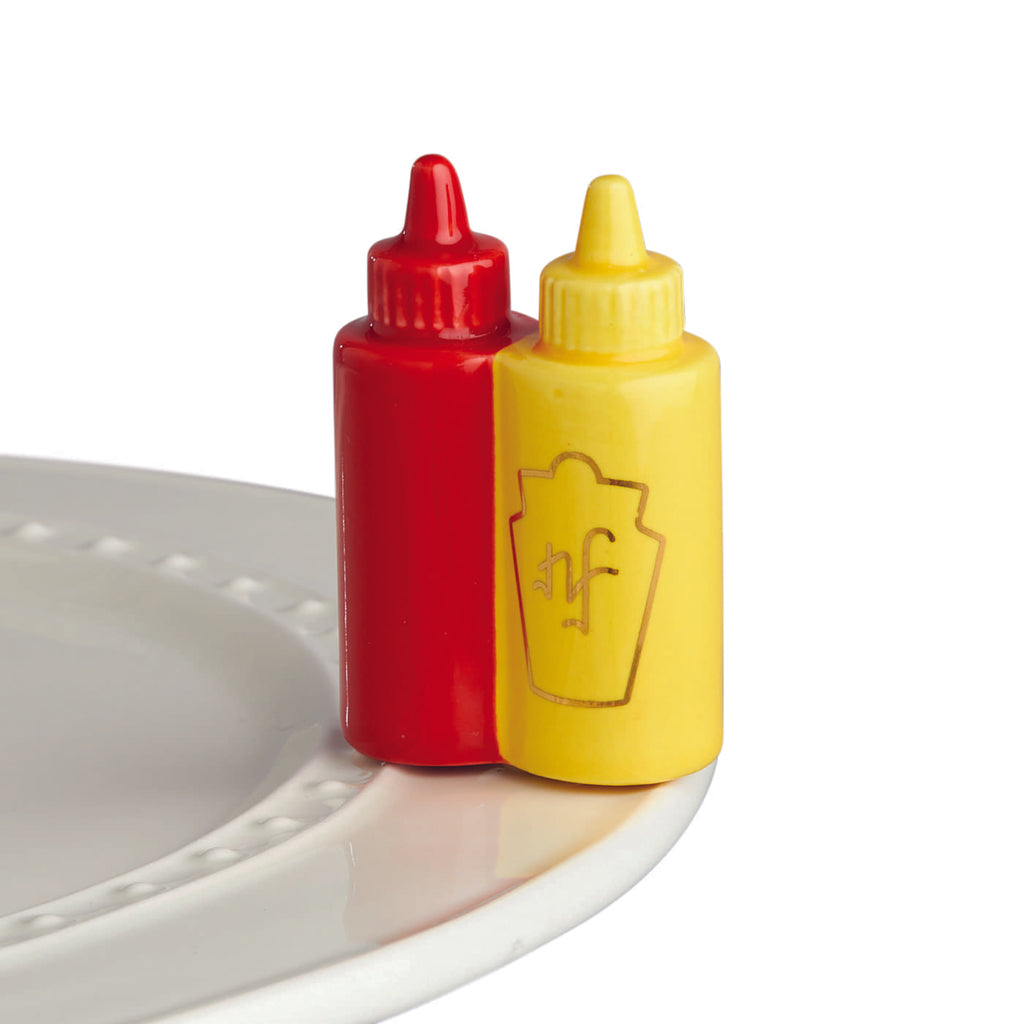 A ceramic ketchup and mustard bottle with gold foil detail attached to the edge of a ceramic tray.