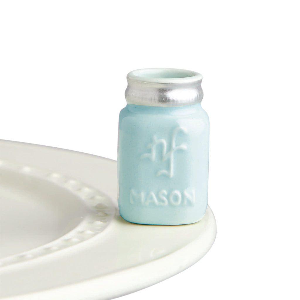 A ceramic mason jar with a light blue finish, attached to the edge of a tray.