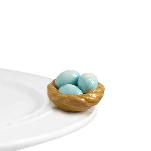 A ceramic nest with light blue eggs in it, attached to the edge of a tray.