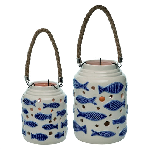 A pair of lanterns (one small, and one tall) on a white background.  Each lantern is white with raised blue fish that have a variety of striped patterns on them.  In between the fish are circles of varying sizes that mimic bubbles and are open to the inside of the lantern, allowing the candlelight to show through.  Each lantern has a handle made of braided jute.