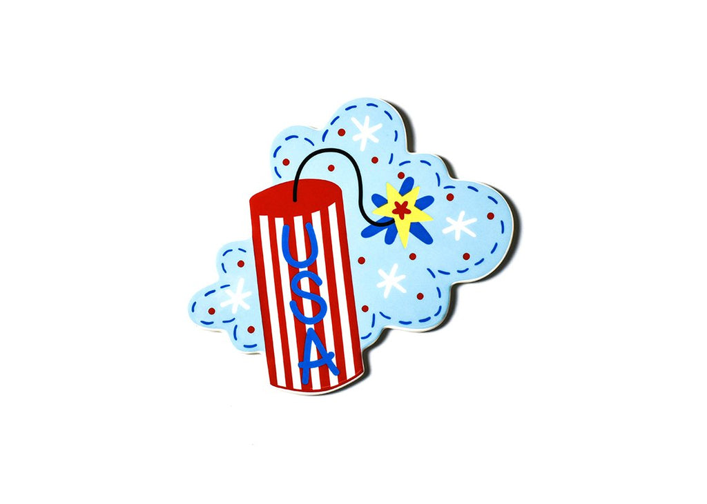 A flat ceramic cutout of a firecracker and fireworks on a blue sky.  The firecracker itself is red and white vertical stripes with blue USA text written vertically.