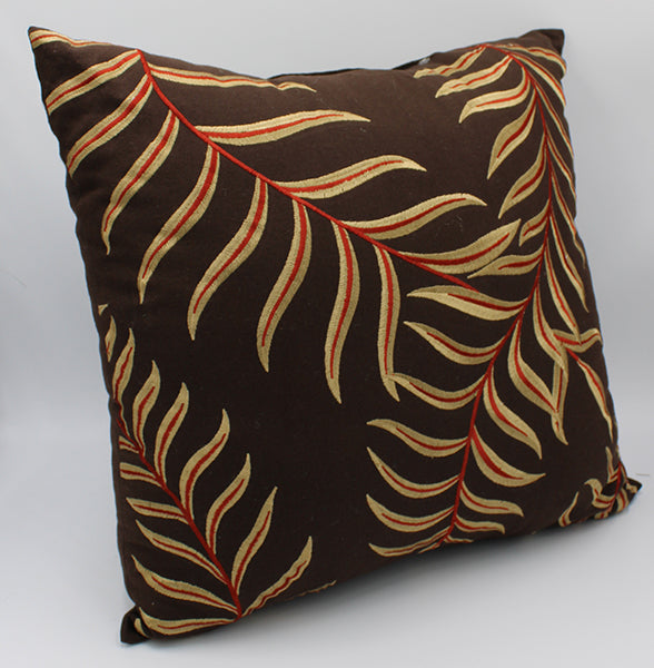 Brown pillow with a tropical leaf pattern embroidered with shiny red and gold thread.