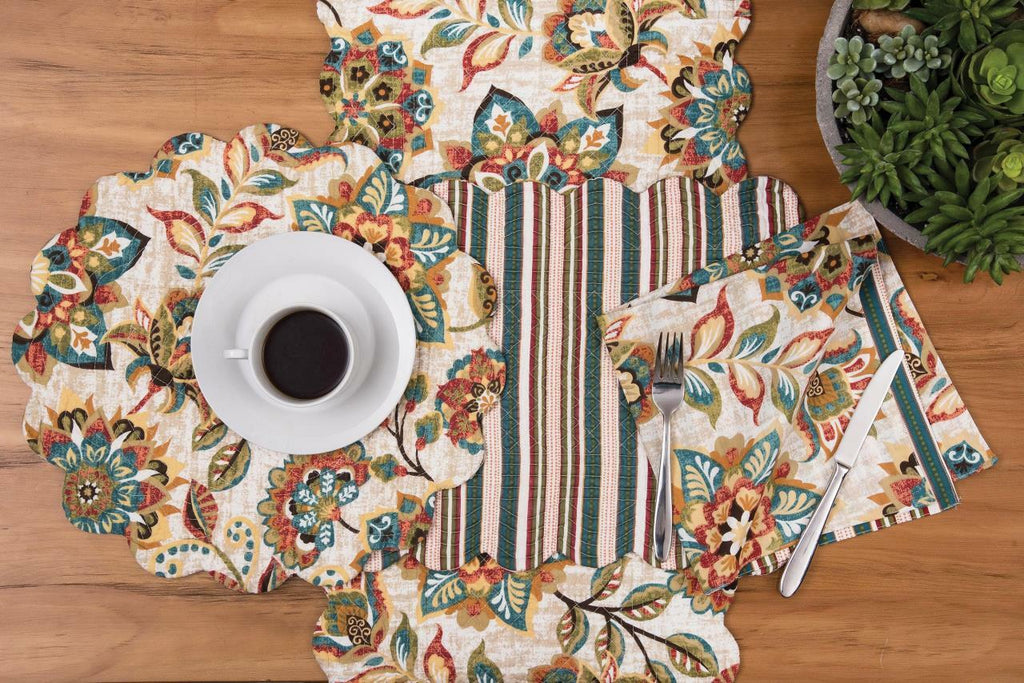A collection of place setting textiles on a wooden background.  Each item has the same multi colored floral pattern of sage blue brown tomato and ochre.  A round scalloped placemat sits on top of a runner and a coordinating square napkin is to the right.
