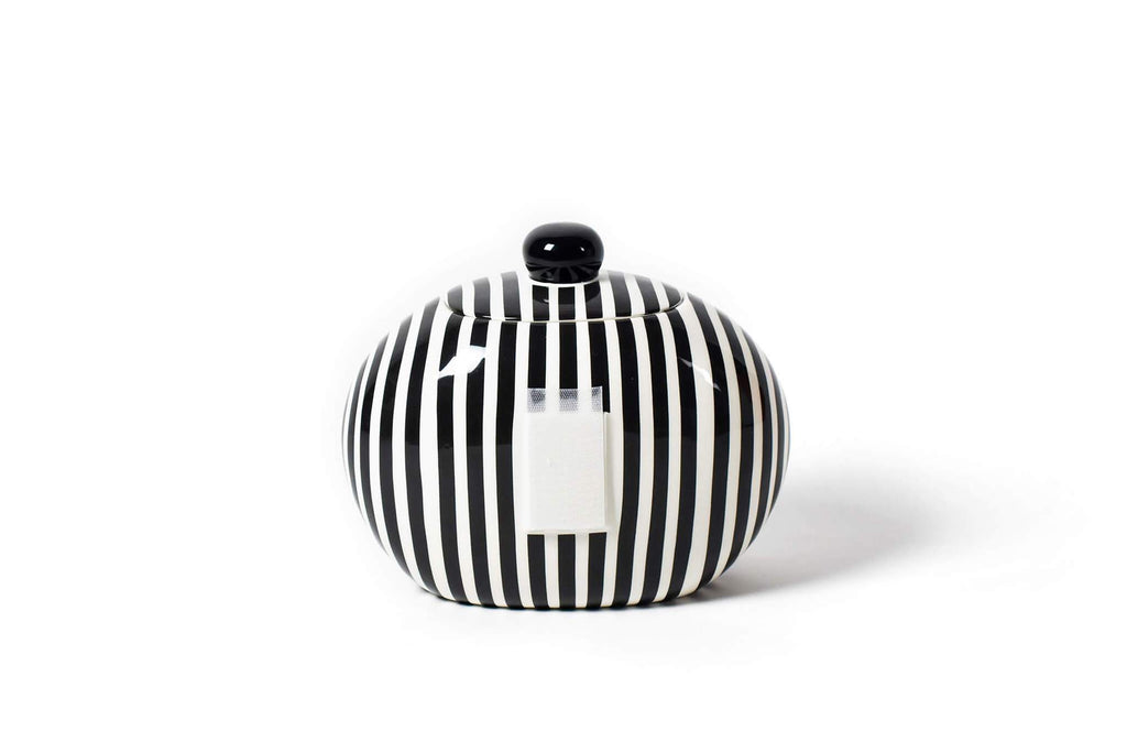 A round cookie jar on a white background.  The body and lid have black and white alternating vertical stripes that are slightly uneven to give a hand painted feel.  The top of the lid has a round black spherical knob for easy lifting.  There is a large piece of velcro on the front to receive decorative attachments.