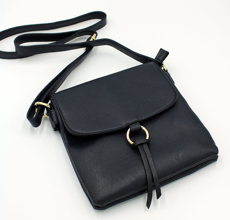 Black square purse with long strap and flap.  Flap has a round brass circular detail with a leather tassel tied to it.