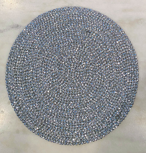 Silver beaded round placemat.  Beads are arranged in a circular pattern following the shape of the placemat.  Placemat is on a white marble surface.