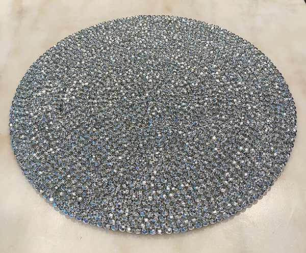 Silver beaded round placemat.  Beads are arranged in a circular pattern following the shape of the placemat.  Placemat is on a white marble surface.