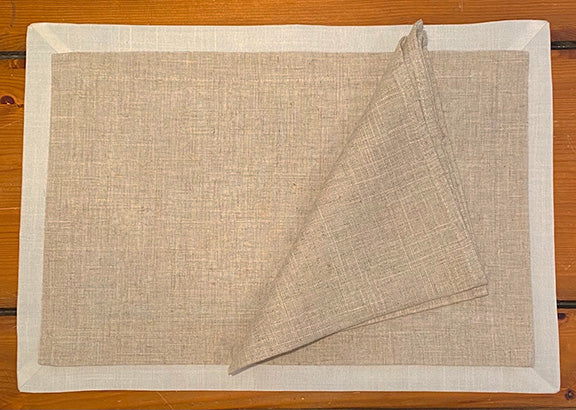 Linen napkin and placemat on a wooden table.  Placemat has a cream border around the natural linen center.