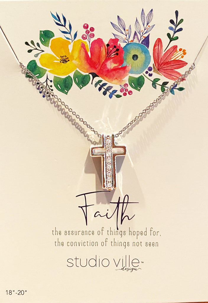 An image of a silver chain necklace with three silver pendants on it, on a card with art of flowers and text that reads 'Faith the assurance of things hoped for, the conviction of things not seen. Studioville design.'  The three silver pendants on the chain form a Catholic cross when they are together, with a vertical row of cubic zirconias in the middle.