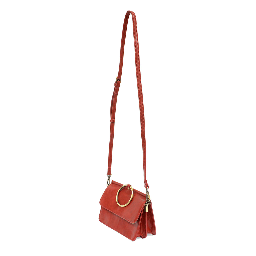 Red leather bag with large metal brass ring with extra long strap, from a slight angle to see the side.