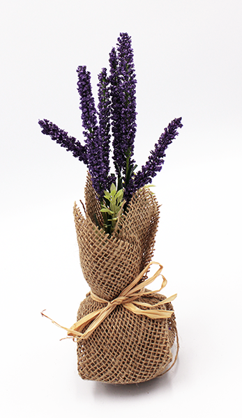 Posable lavender stems and mixed greens are fixed in a foam base wrapped in burlap and finished with a jute bow.