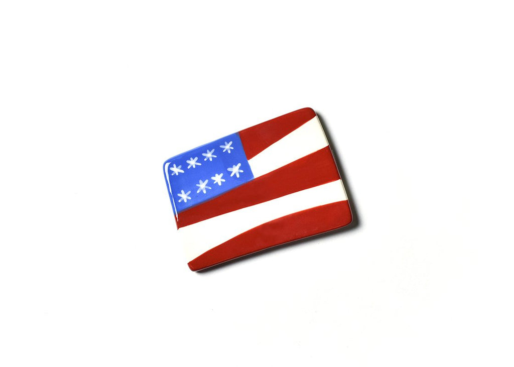 A flat ceramic cut out of a flag with a blue portion in the upper left, and red and white alternating stripes over the rest.  In the blue portion are white asterisks mimicking stars.  The shape of the piece isn't exactly square, the top is narrower than the bottom, and the left side is shorter than the right.