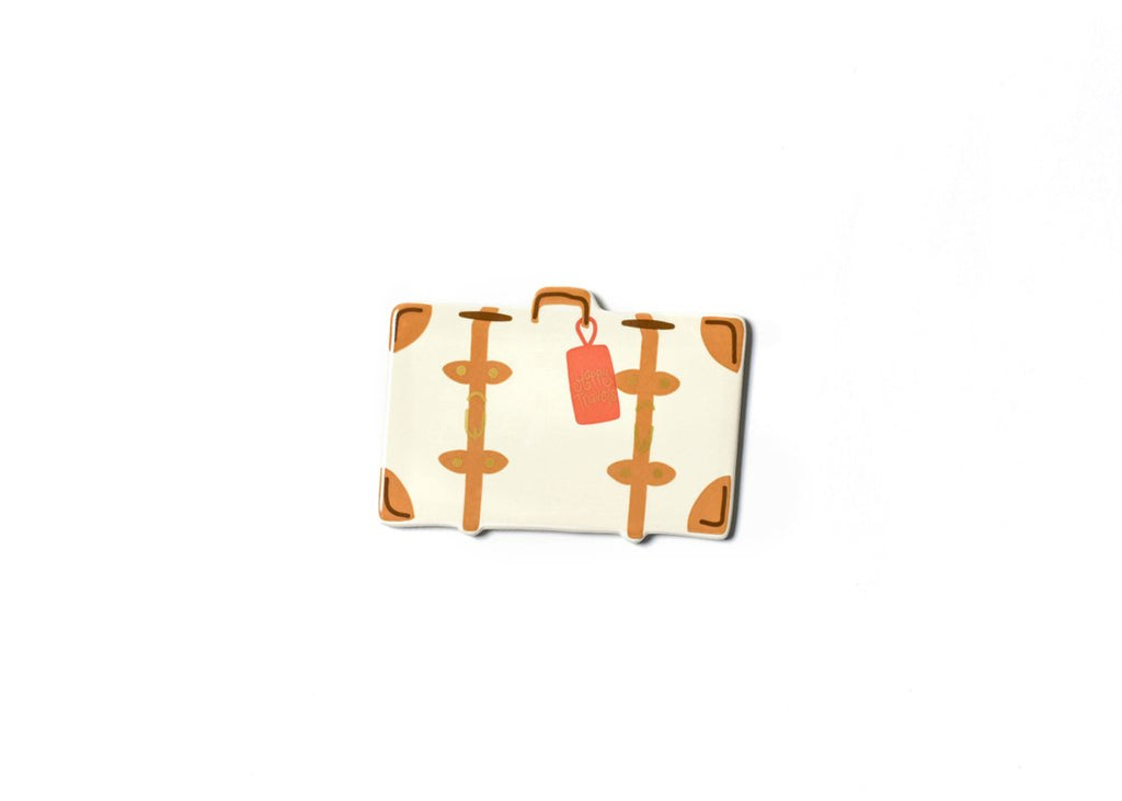 A flat ceramic cut out of a cream colored suitcase with tan corners, straps and handle.  There is a coral colored tag hanging off the handle with the words 'Happy Travels' in gold.