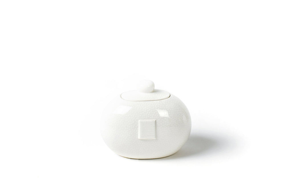A round cookie jar on a white background.  The outside of the jar is slightly off white with a micro white polka dot pattern all over that extends onto the lid.  The lid is topped with a spherical white orb.  The front of the jar has a large piece of velcro on it to receive decorative attachments.