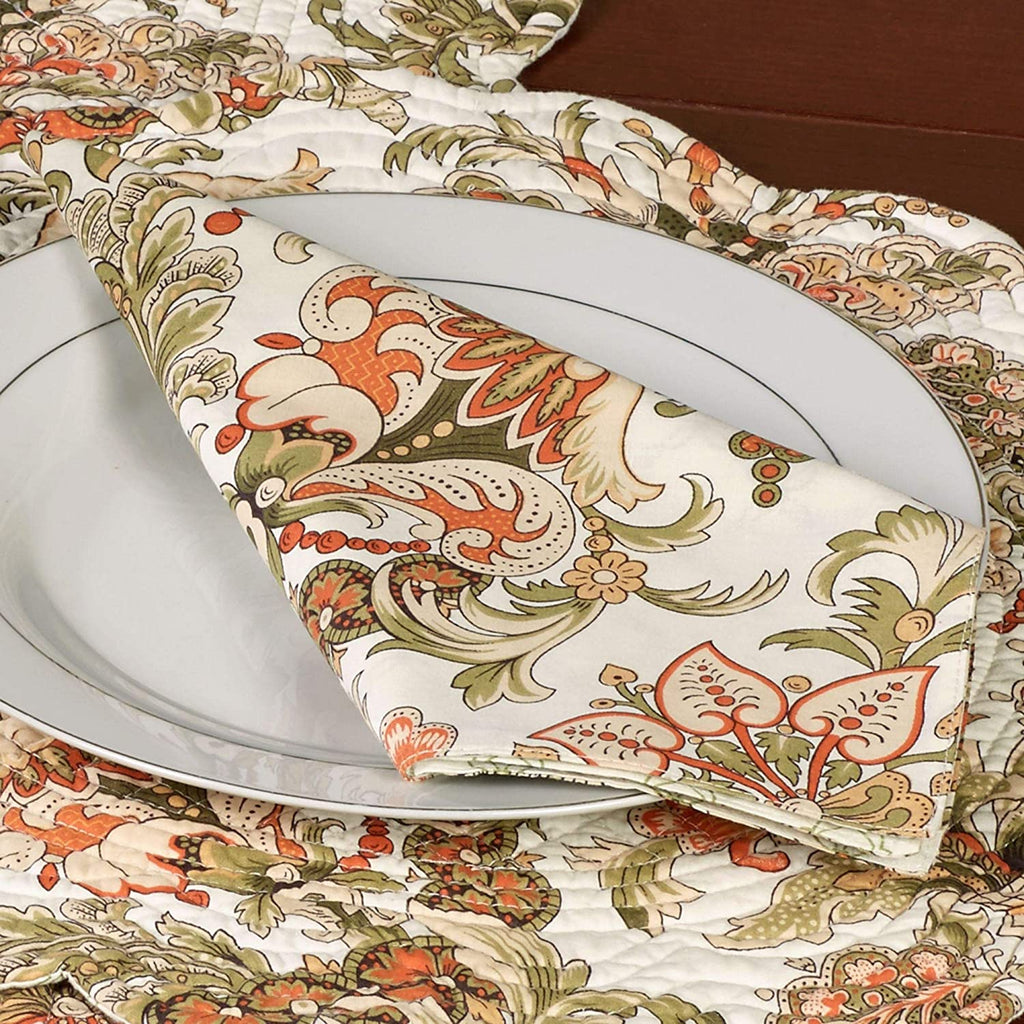 Jacobean flourish design printed on a cotton napkin in tan, green and orange.  Napkin is folded and placed on a white plate.  Plate is placed on a coordinating placemat with scalloped edges.
