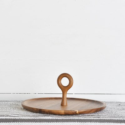 Wooden tray with central ring handle sitting on a striped runner in front of a white wall.