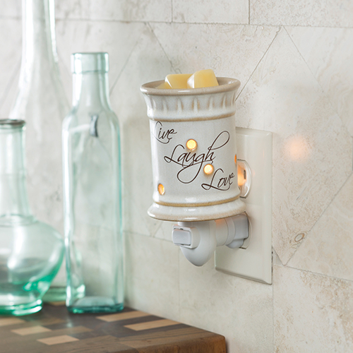 Ceramic cylinder candle warmer plugged into an outlet.  Live Laugh Love is written on the side in a cursive script.  The outlet is on a tiled wall and behind the warmer are three tall glass vases.