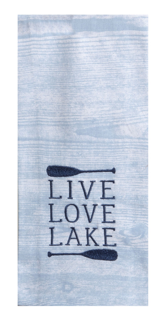 The front of a kitchen towel that has a printed pattern of wood grain in a blue hue, which looks similar to ripples in water.  Towards the bottom are navy embroidered horizontal canoe paddles with text in-between that says 'live love lake', each on separate lines.